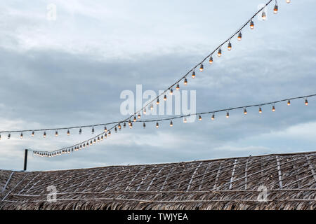 Antique light bulbs decorative hanging on wire over thatched roof Stock Photo