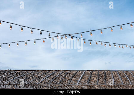 Antique light bulbs decorative hanging on wire over thatched roof Stock Photo