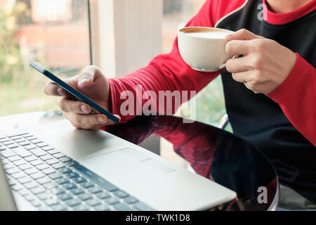 Casual man drinking coffee with using smartphone with laptop in cafe Stock Photo