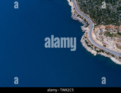 Aerial landscape of coastline and a road seascape. Car drives down the empty asphalt road running along the sunny Mediterranean shoreline of Turkey. Stock Photo