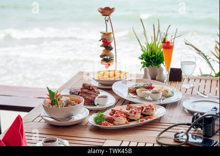 Food with Shrimp spicy, Fried pork ribs, Tom yum goong, Beef steak on wooden dining table on restaurant patio in tropical sea Stock Photo