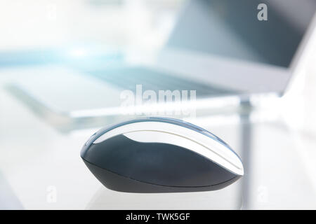 Computer wireless mouse on glass desk with notebook in the background Stock Photo