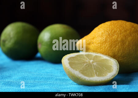 One Whole Lemon with a Sliced Lemon in front of Whole Limes on a Blue Background Stock Photo