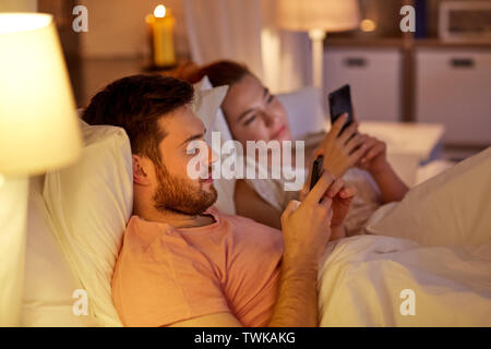 couple using smartphones in bed at night Stock Photo