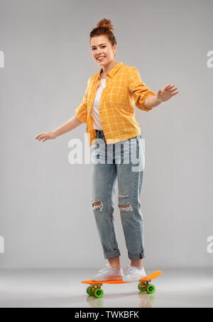 red haired teenage girl riding on short skateboard Stock Photo