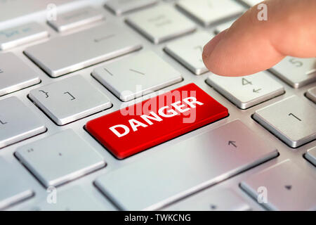 danger word on computer keyboard button. Finger presses the color button on the gray keyboard Stock Photo