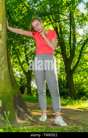 A jogger leans against a tree and measures her pulse with her hand Stock Photo