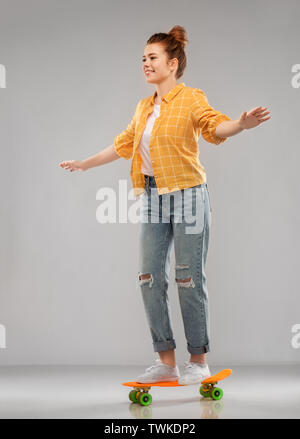 red haired teenage girl riding on short skateboard Stock Photo