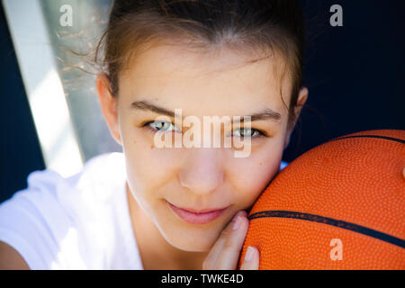 Portrait of a beautiful and young female basketball player with face resting on the ball Stock Photo