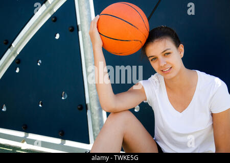 Beautiful female basket player resting on the floor with ball on head Stock Photo