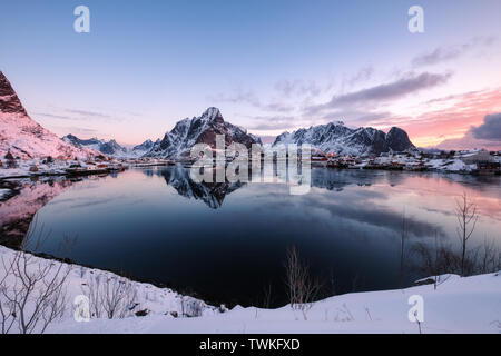 Snowy Scandinavian village with surrounded mountain on coastline at sunrise Stock Photo