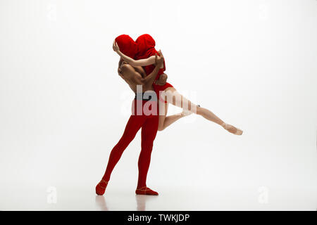 Graceful classic ballet dancers dancing isolated on white studio background. Couple in bright red clothes like a combination of wine and milk. The grace, artist, movement, action and motion concept. Stock Photo