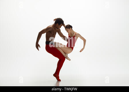 Graceful classic ballet dancers dancing isolated on white studio background. Couple in bright red clothes like a combination of wine and milk. The grace, artist, movement, action and motion concept. Stock Photo