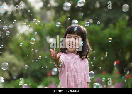 Girl trying to hold floating bubbles Stock Photo