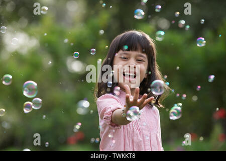 Girl trying to hold floating bubbles Stock Photo