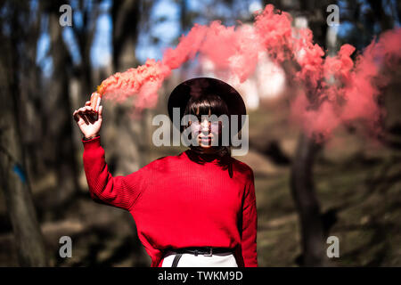 Young woman holding red colorful smoke bomb on the outdoor park.Red smoke spreading in the cerebration festival. Stock Photo