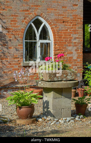 Stone trough. Mounted on a breeze block plinth and a mill stone. Now used as a plant container garden ornament. Raised above ground level to frustrate rabbits, and reduce slug and snail damage to sensitive cultivated plantings.​ Stock Photo
