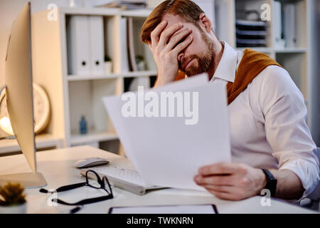 Mid age businessman tired of working with the documents in the evening office Stock Photo