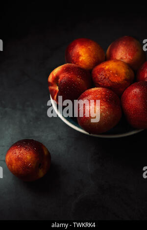Still life of fresh delicious sweet nectarines with droplets of water in a bowl on dark background. Low key. Stock Photo