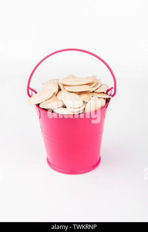 Heap pumpkin seeds in pink bucket on white background. Copy space Stock Photo