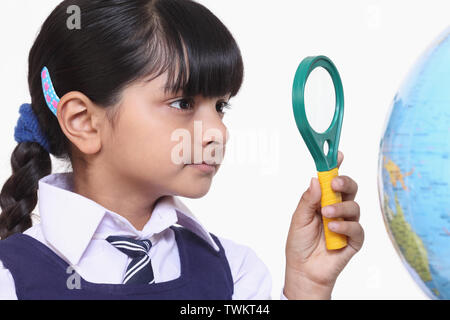 Girl looking through magnifying glass at a globe Stock Photo