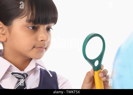 Schoolgirl looking at magnifying glass at a globe Stock Photo