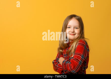 Portrait of a funny little blond girl in a red dress on a yellow background. Stock Photo
