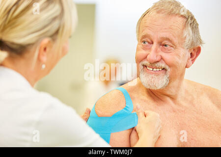 Senior patient is pleased about Kinesio taping on his shoulder in the physiotherapy Stock Photo