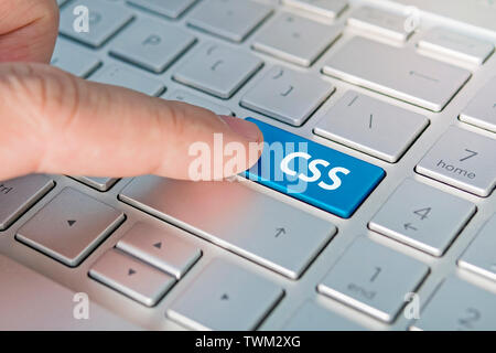 CSS computer language. The writing on button modern of gray laptop. Finger presses the button. Programmer for work. Stock Photo