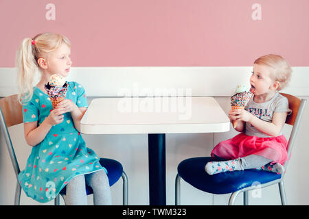 Lifestyle portrait of two happy Caucasian cute adorable funny children girls sitting together bragging boasting their ice-cream. Love envy jealous sis Stock Photo