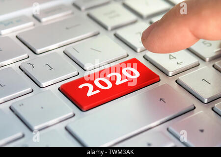Keyboard with text 2020 and finger pushing the enter button. Color button on the gray silver keyboard of modern ultrabook. caption on the button. Stock Photo