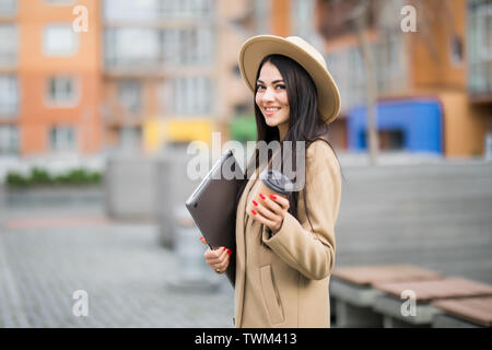 pretty young business woman holding a cup of coffee and files walking on the street Stock Photo