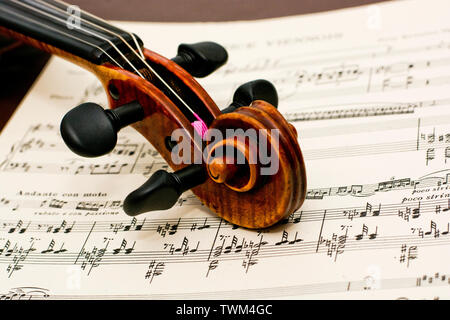 Violin neck of this classic vintage wooden instrument lying down on top of classical sheet music notes on table Stock Photo