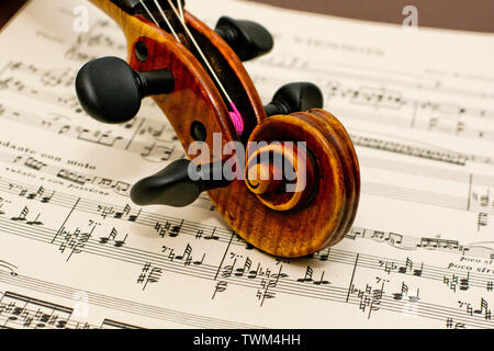 Violin neck of this classic vintage wooden instrument lying down on top of classical sheet music notes on table Stock Photo