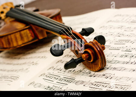 Violin neck of this classic vintage wooden instrument lying down on top of classical sheet music notes on table Stock Photo