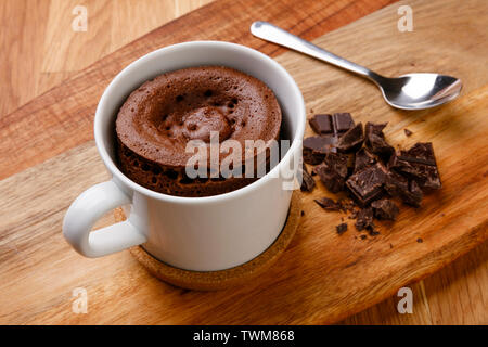Delicious chocolate sponge pudding shot on a wooden board with a hand full of fudge pieces, in a cup with a spoon. Stock Photo
