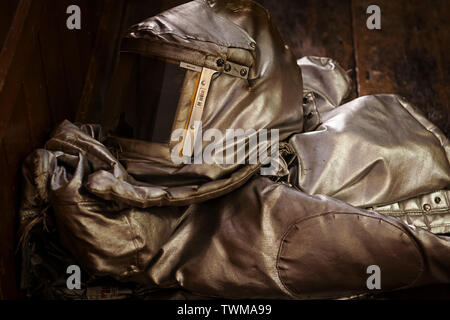 A folded up slightly damaged fire proximity suit also known as a bunker suit on a wooden floor. There is a visible hole in the visor of the suit. Stock Photo