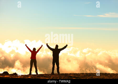 Success, achievement and accomplishment concept with hiking people cheering and celebrating of joy with arms raised outstretched up in the sky on trekking hike outside. Hikers having fun at sunset. Stock Photo