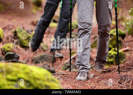 Hiking - Hikers walking in forest with hiking sticks on path trail in mountains. Close up of hiking shoes and boots. Man and woman hiking together. Stock Photo