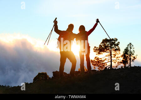 Success, achievement and accomplishment concept with hiking people cheering and celebrating of joy with arms raised outstretched up on trekking hike outside. Hikers having fun at sunset. Stock Photo
