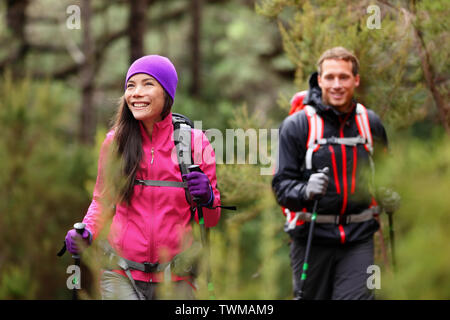 Hiking people - hikers trekking in forest on hike. Couple on adventure trek in beautiful forest nature. Multicultural Asian woman and Caucasian man living healthy active lifestyle in woods. Stock Photo