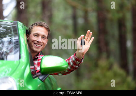 Car driver showing car keys and thumbs up happy. Young man holding car keys for new car. Rental cars or drivers licence concept with male driving in beautiful nature on road trip. Stock Photo