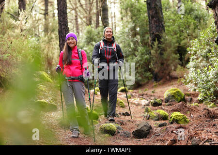 Hiker couple backpackers hiking in forest on path in mountains. Multiracial woman and man living healthy active lifestyle enjoying nature in La Esperanza forest, Tenerife, Canary Islands, Spain. Stock Photo