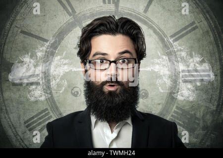 bearded surprised man, blowing steam coming out of ears, over clock background, concept of transience of time, fatigue from lack of hours in a day Stock Photo