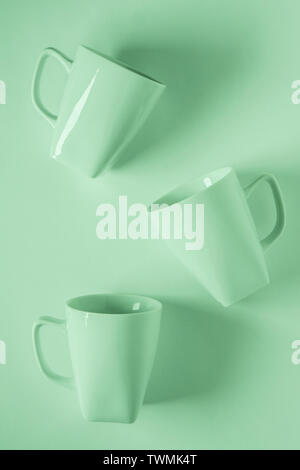 3 monochromatic green coffee mugs scattered on green background with blank empty room space for text, copy, or copyspace. Modern top view concept of t Stock Photo