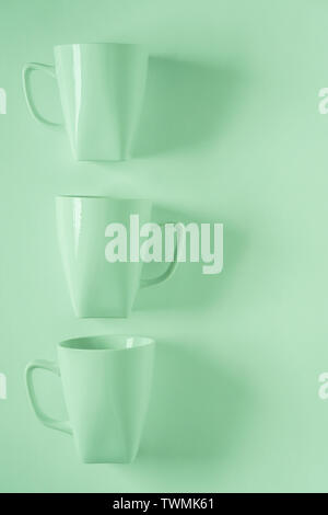 3 monochromatic green coffee mugs lined up in a row on green background with blank empty room space for text, copy, or copyspace. Modern top view conc Stock Photo