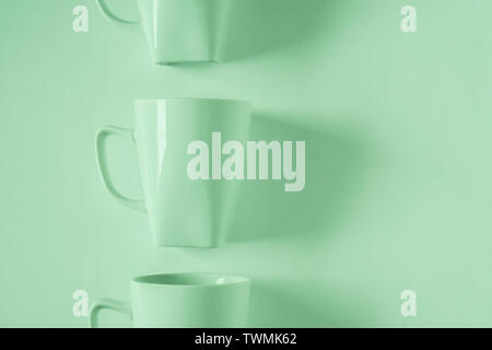 One singled out monochromatic green coffee mug lined up in a row on green background with blank empty room space for text, copy, or copyspace. Modern Stock Photo