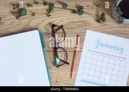 High-angle shot of a home office desk space with a plant, notebook, glasses and a calendar with pen Stock Photo