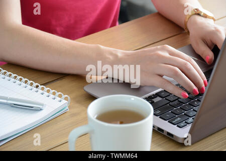 Young woman with a neat pink manicure using modern laptop. With cup of tea and notebook. Stock Photo