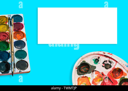 Watercolor paints and a palette with spots on a blue background. Paint brush in the paint. The concept of drawing, art, creativity. Artistic tools Stock Photo